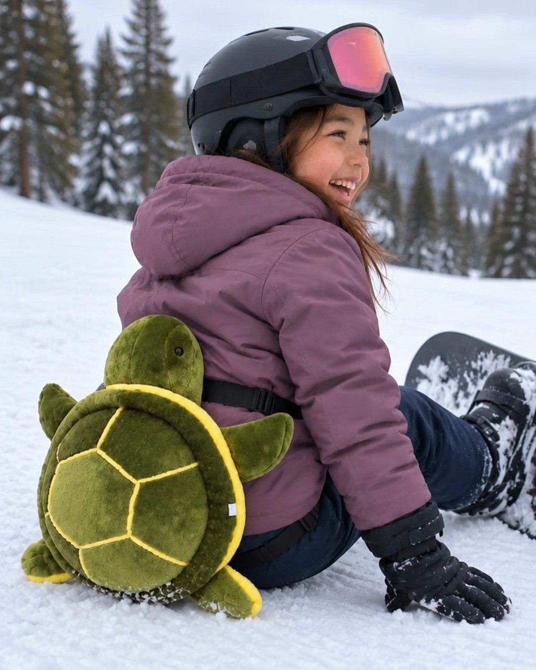 Kid sitting in the snow on the turtle bum pad, laughing